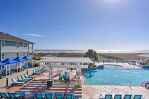A pool area with sun loungers and umbrellas, a covered seating area, and a view of the ocean. - Walk to Beach: Condo w/ Bay View in Galveston (Galveston)