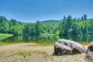A serene lakeside scene with a dock, large rocks, and dense forest.