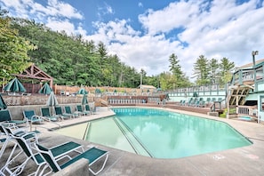 A swimming pool with lounge chairs and umbrellas, surrounded by a wooden deck and trees.