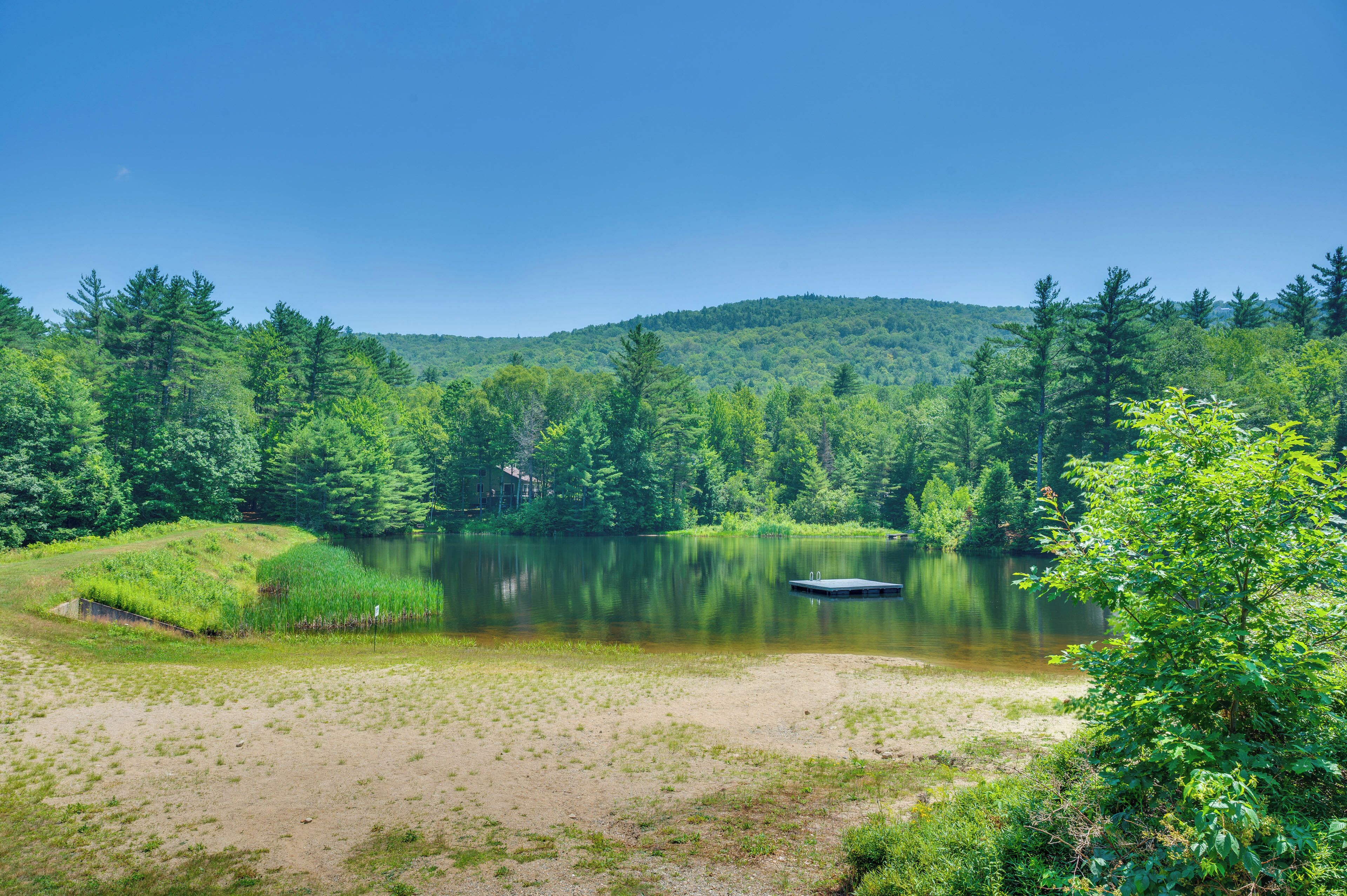 A serene lakeside view with a dock, surrounded by dense forest and hills.
