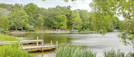 A serene lakeside setting with a wooden dock, lush greenery, and a small boat docked on the water.