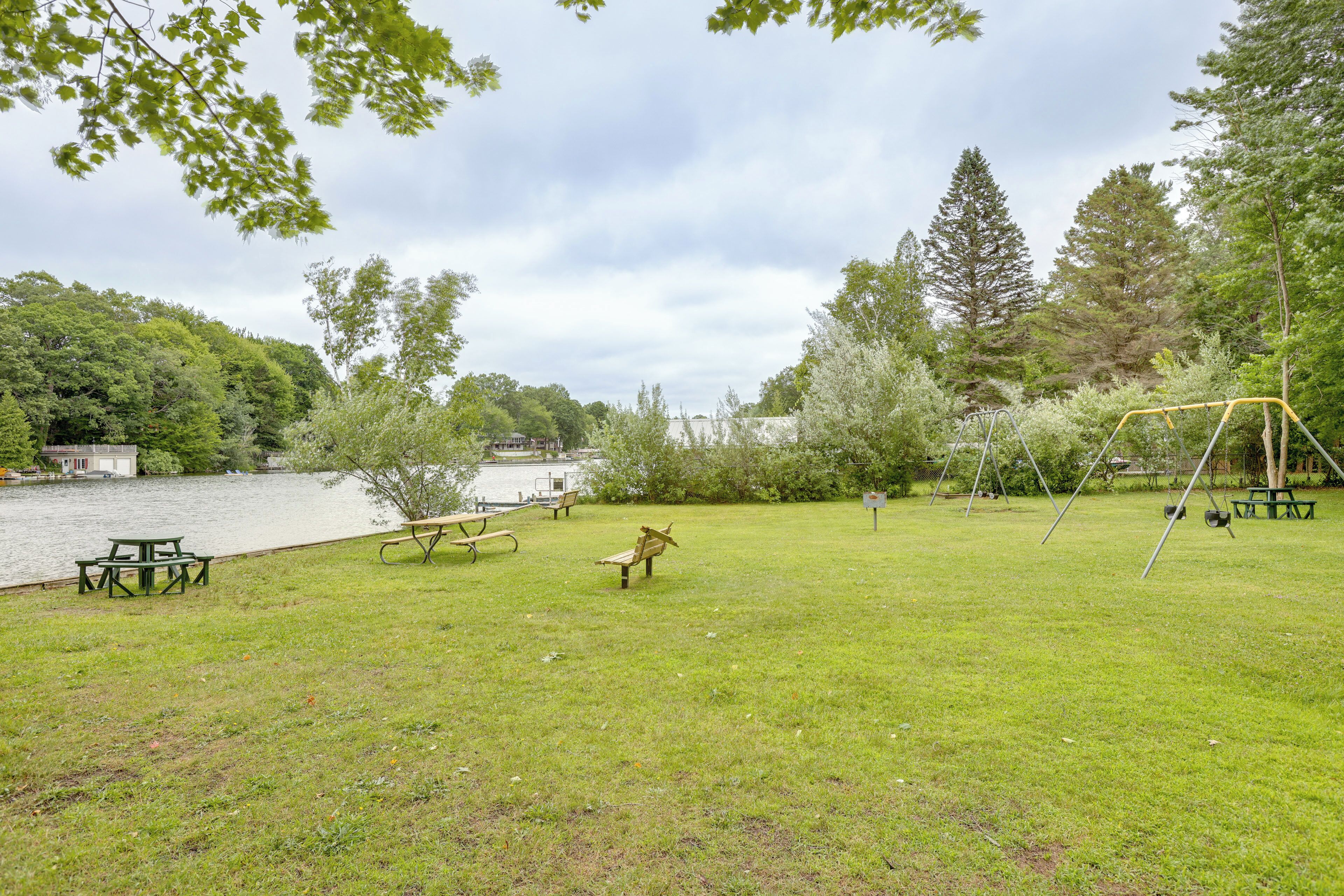 A grassy park area with picnic tables, a swing set, and a lake in the background.