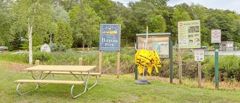 A picnic table, a sign for Hamlin Township South Bayou Park, and informational signs about invasive species.