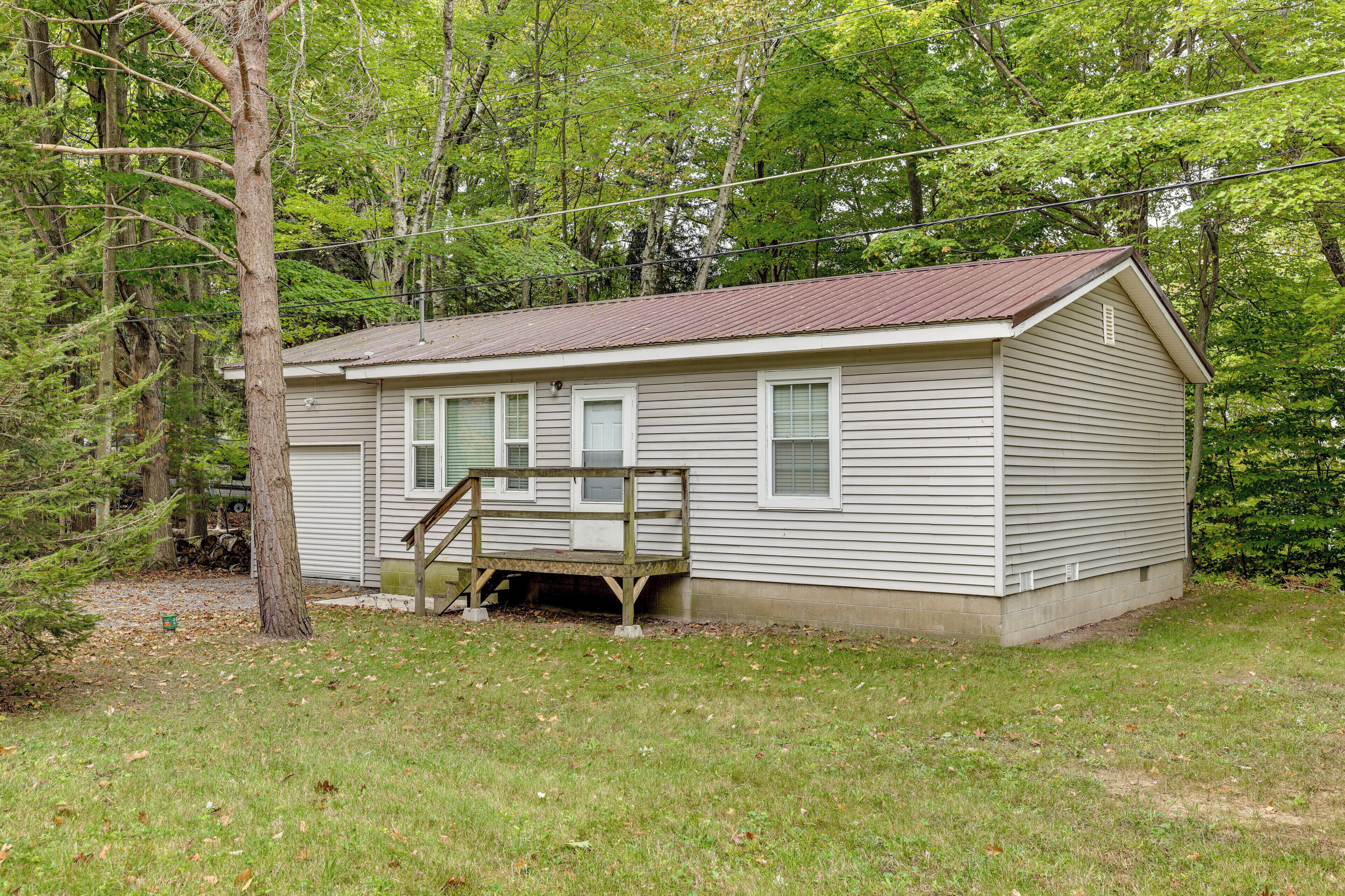A single-story cabin with a wooden deck, surrounded by trees and a grassy yard.
