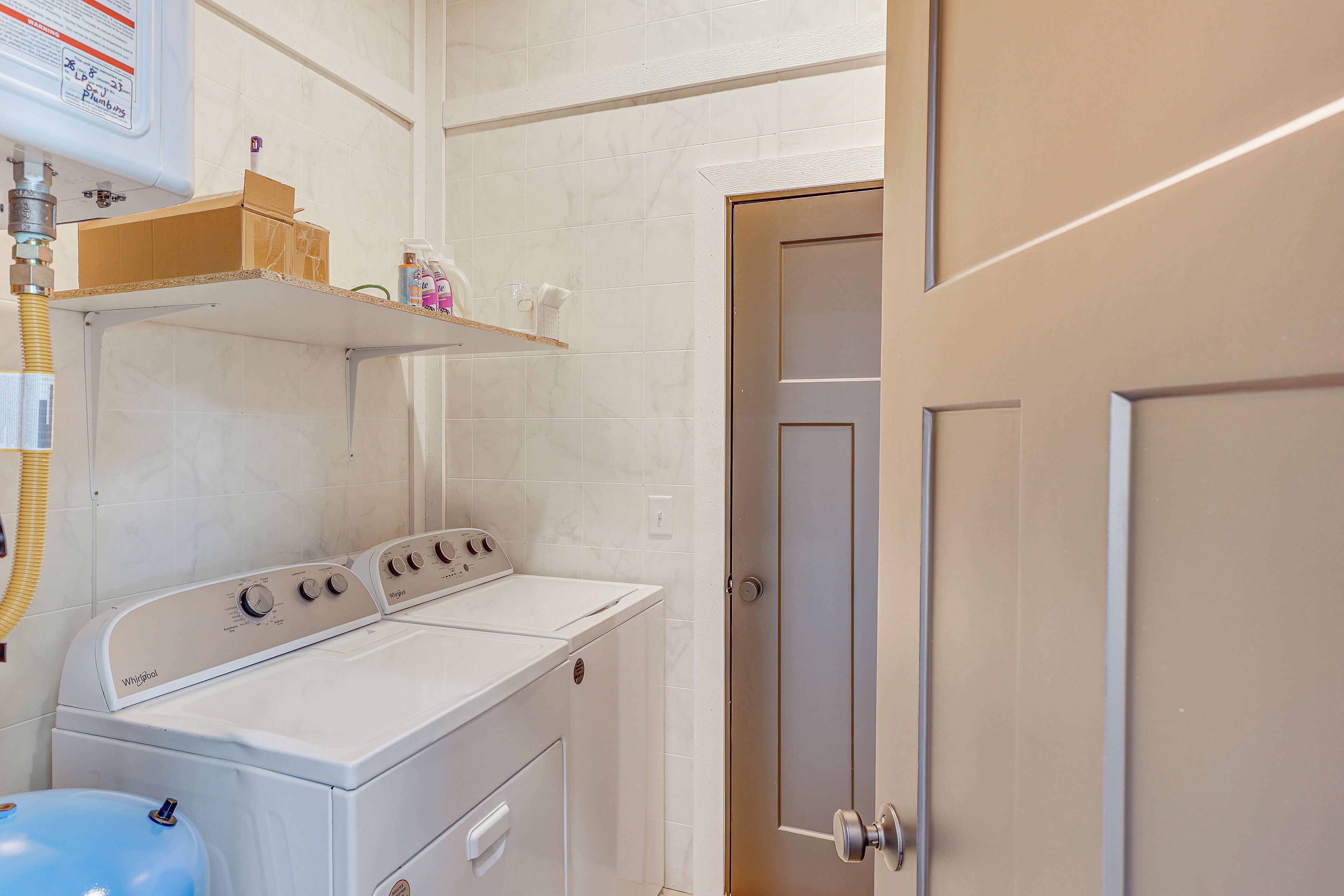 A laundry area with a front-loading washer and dryer, a water heater, and a shelf with toiletries.