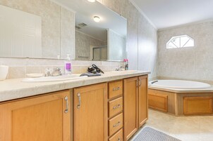 Un baño con un espejo grande, armarios de madera, un lavabo y una bañera.