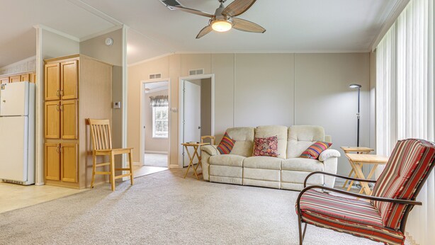 A living room with a beige sofa, a striped armchair, a wooden cabinet, and a ceiling fan. - Walk to Scenic Trails: Waterfront Okeechobee Oasis (Okeechobee)
