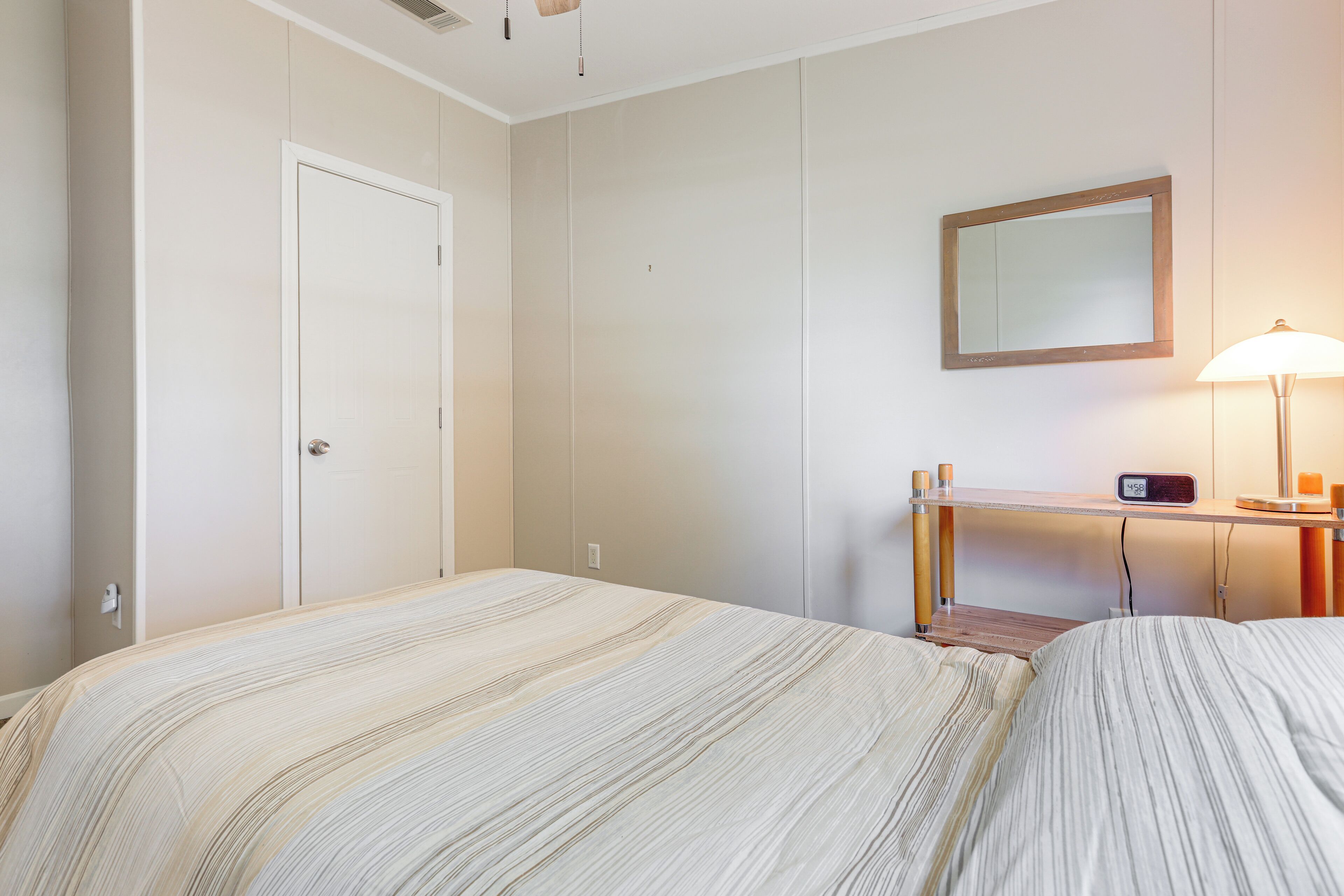 Ett hotellrum med en säng, ett skrivbord med en lampa, en spegel och en dörr.