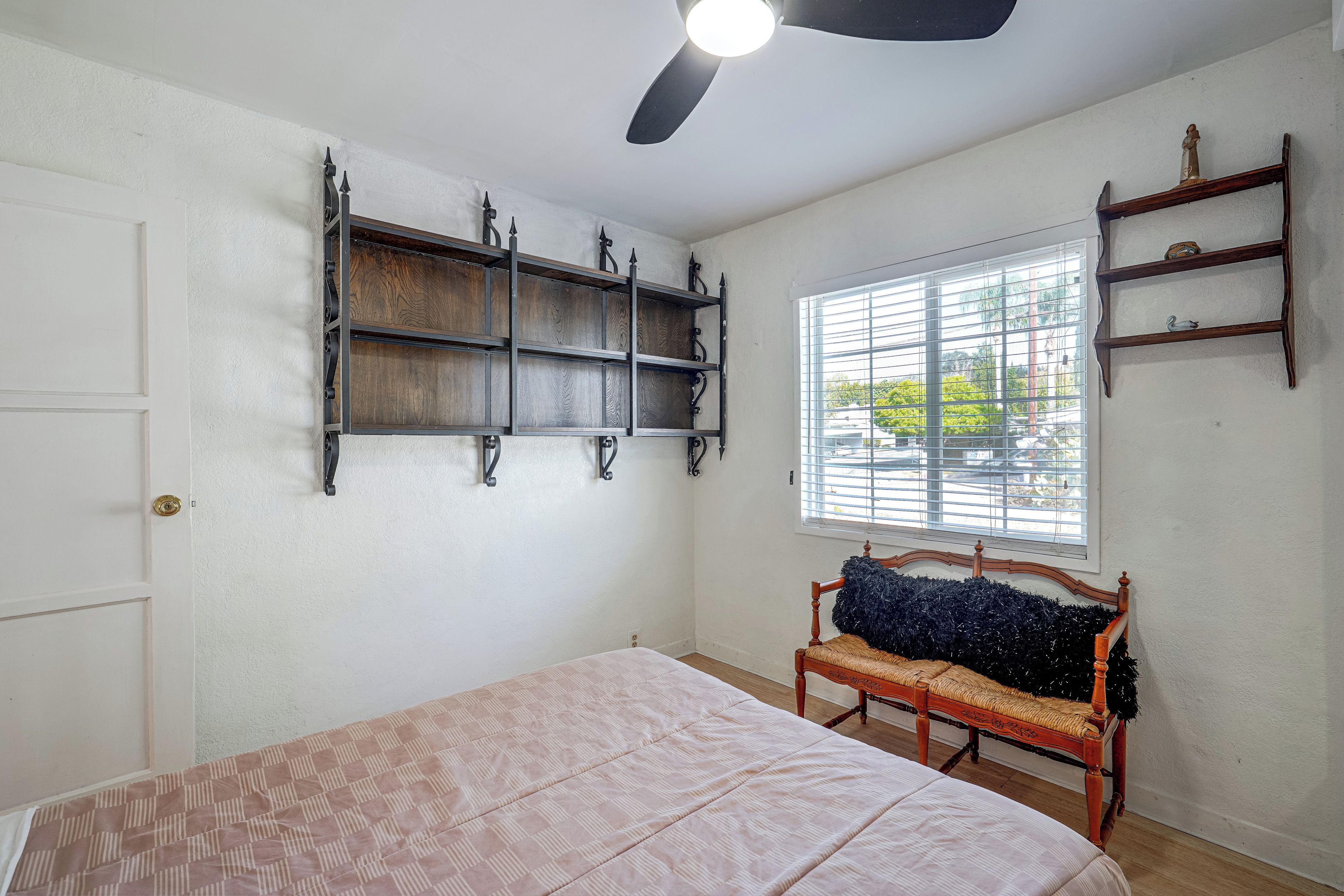 A bedroom with a bed, a wooden chair, a window with blinds, and a ceiling fan.
