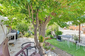 A patio area with a dining table and chairs, surrounded by potted plants and a tree.