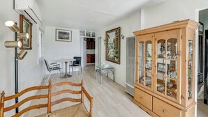 A room with a wooden bed, a glass cabinet, a dining table with chairs, and a white air conditioner. - Fullerton Home Base: Easy Access to Dtwn + Csuf! (Fullerton)