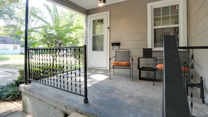 A covered porch with a concrete bench, two metal chairs with orange cushions, a black metal railing, and a white door with a window. - Updated North Greenwood Cottage < 1 Mi to Dtwn! (Greenwood)