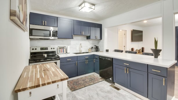 A modern kitchen with dark blue cabinets, a white countertop, and a wooden table. - Updated North Greenwood Cottage < 1 Mi to Dtwn! (Greenwood)