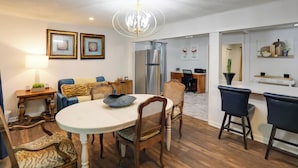 A dining area with a round table, wooden chairs, a chandelier, and a kitchen in the background. - Updated North Greenwood Cottage < 1 Mi to Dtwn! (Greenwood)