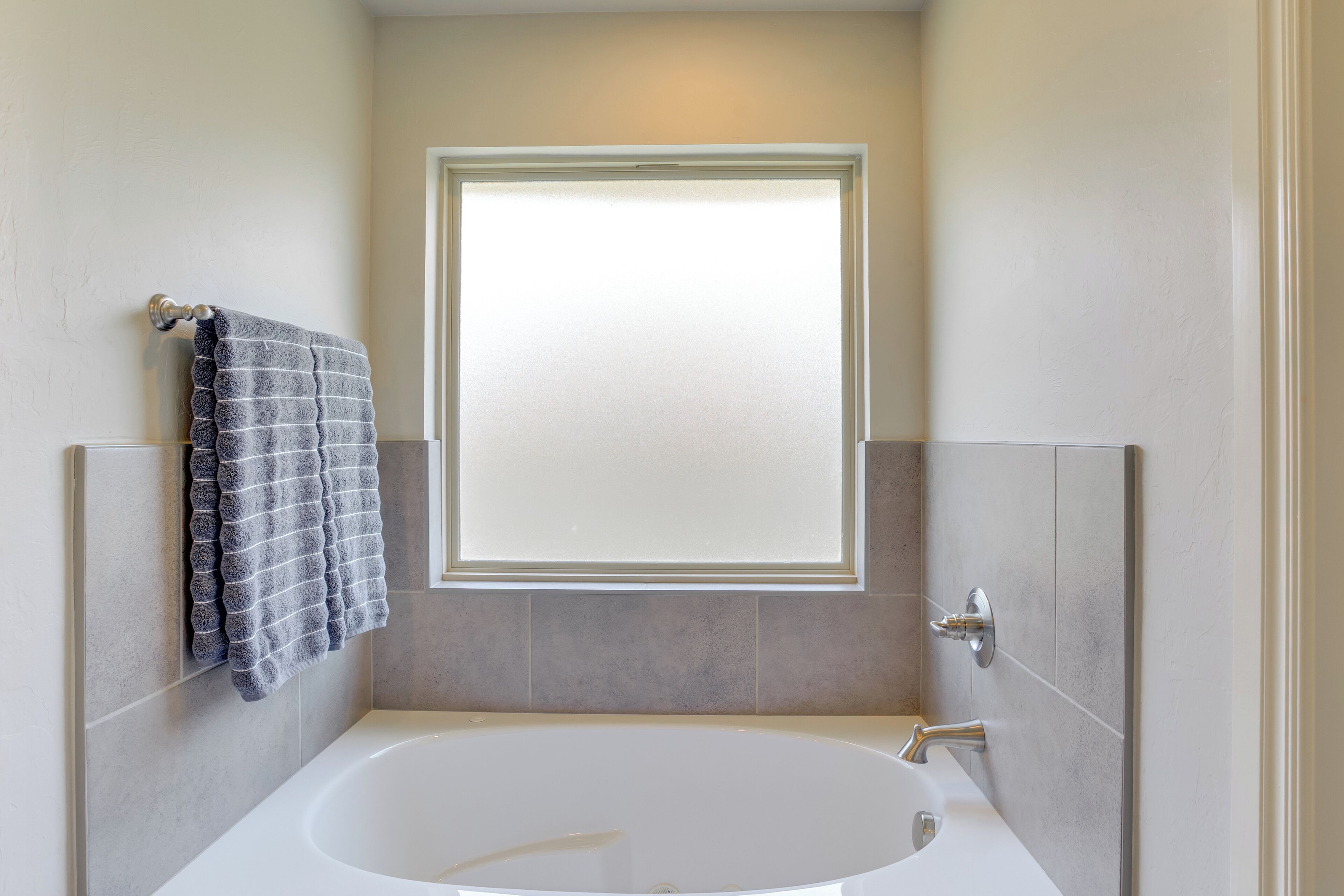 A bathroom with a large bathtub, a towel rack with a towel, and a window with frosted glass.