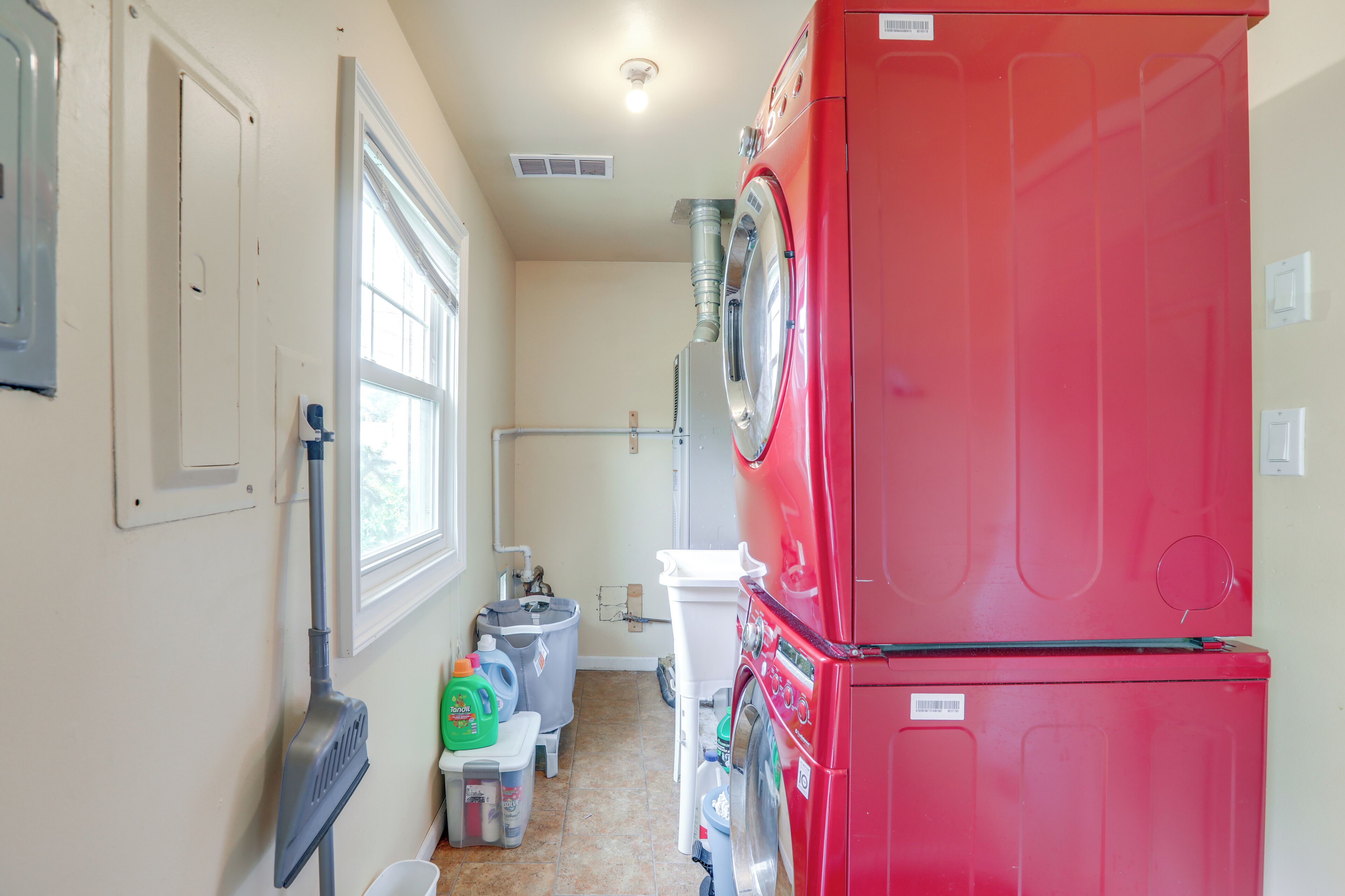A laundry room with a red washing machine, a mopping bucket, and cleaning supplies.