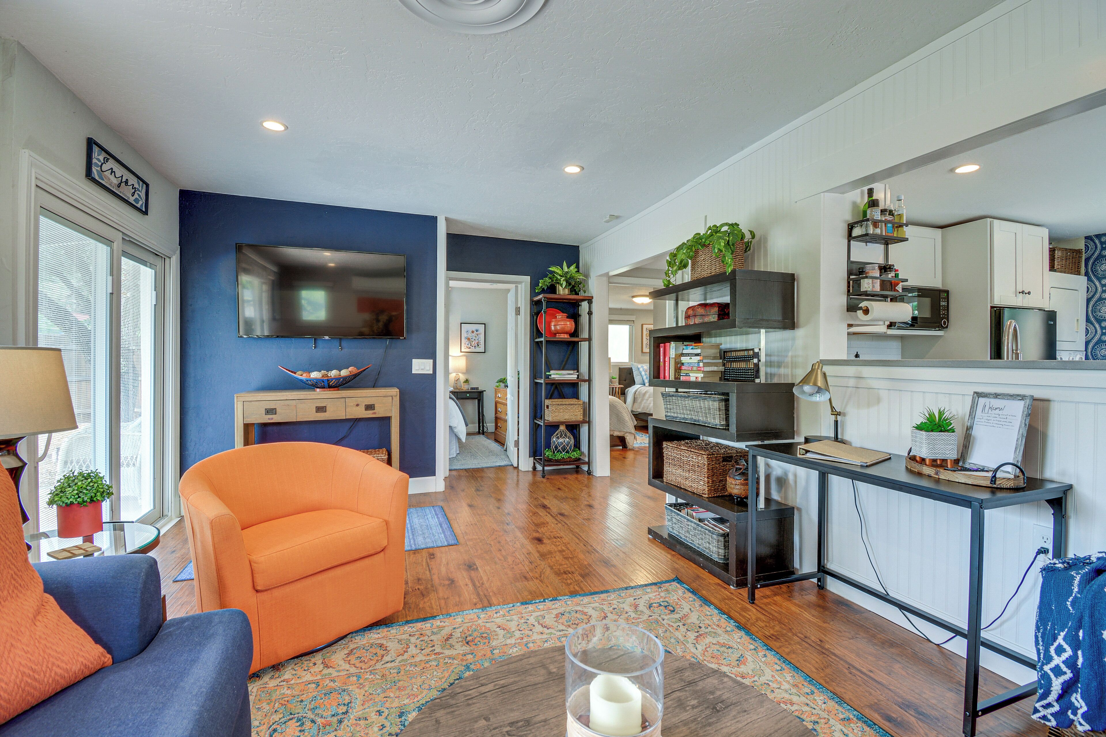 Un salon moderne avec un mur d’accent bleu, un plancher en bois et un mélange de meubles, notamment un canapé, un fauteuil et une table basse sur laquelle est posée une bougie.