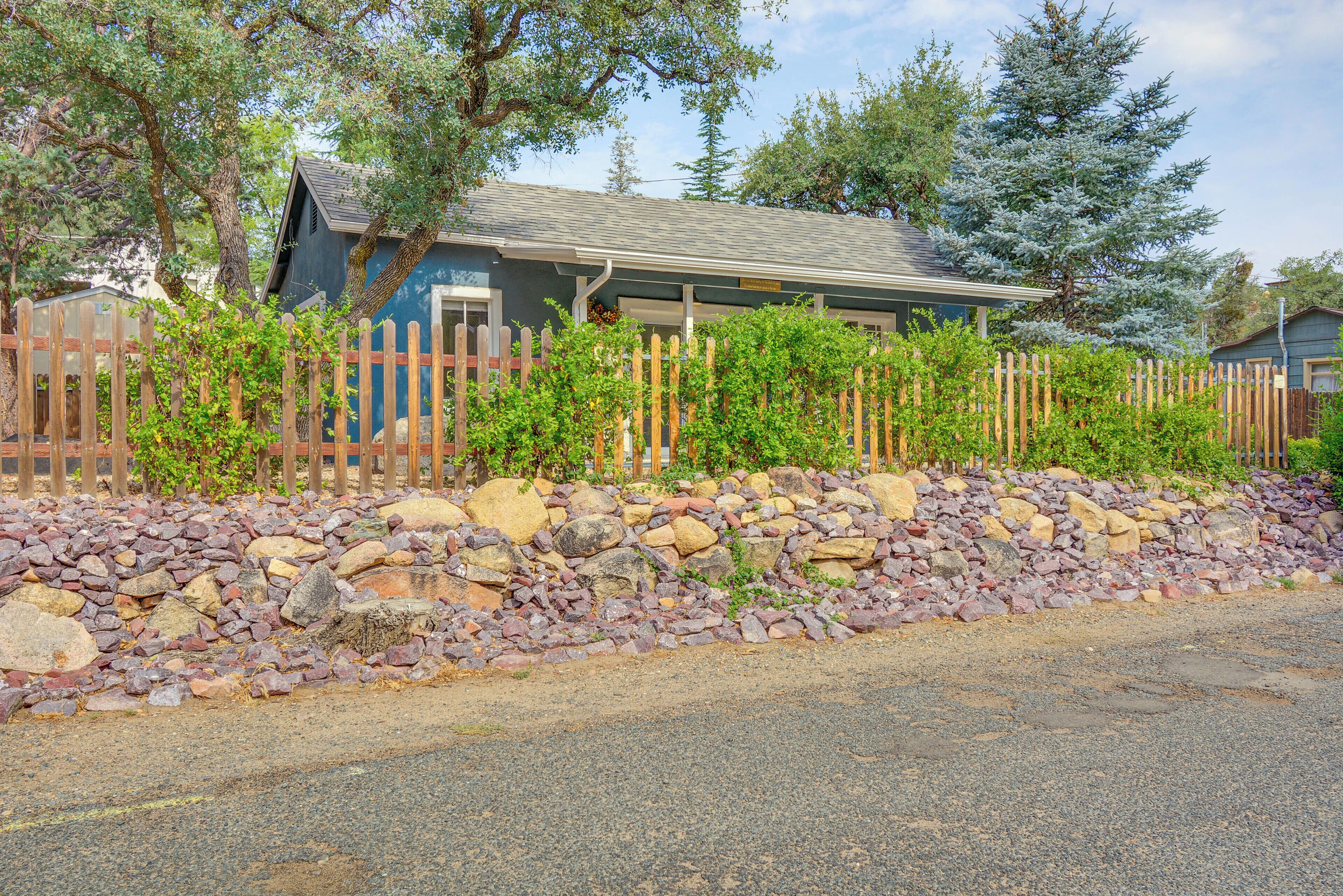 A house with a stone wall and wooden fence, surrounded by trees.