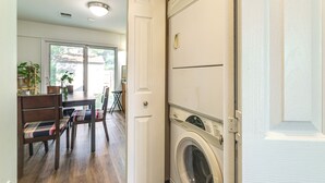 A laundry room with a front-loading washer and dryer, wooden chairs, a dining table with chairs, and a view through a glass door to the outside. - 3 Mi to Dulles Airport: D.c. Area Townhome (Herndon)