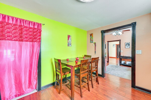 A dining area with a wooden table and chairs, a bright green wall, and a pink curtain.