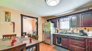 Una cocina compacta con armarios de madera, un refrigerador de acero inoxidable y una zona de comedor con una mesa y sillas de madera.