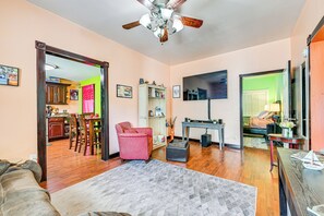 A living room with a ceiling fan, a TV, a dining area with chairs, and a kitchen visible through an open doorway. - Close to Airport: Home in the Heart of Charlotte! (Charlotte)