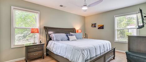 A bedroom with a bed, nightstands, a ceiling fan, and windows.