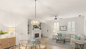 A spacious living area with a glass dining table, wicker chairs, a sofa, and a fireplace. - Charming Condo Across the Street from the Beach (St Simons Island)