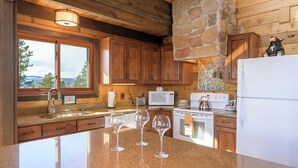 A kitchen with wooden cabinets, a stone wall, a refrigerator, a stove, and three wine glasses on the counter. - 273 Fallen Rock BIG Views 4 Bed Home, Pet Friendly + Hot Tub! (Tabernash)