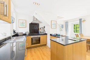 A modern kitchen with wooden cabinets, a central island, and a built-in oven. - Host & Stay | Dove Cottage (Warkworth)