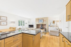 A modern kitchen with wooden cabinets, a central island, and a stone fireplace. - Host & Stay | Dove Cottage (Warkworth)