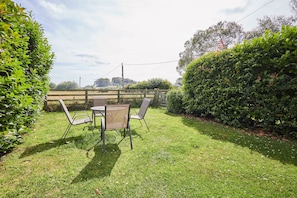 A grassy outdoor area with a table and chairs, surrounded by hedges and a wooden fence. - Host & Stay | Dove Cottage (Warkworth)