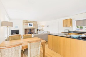 A modern kitchen with a central island, wooden cabinets, and a dining area with wicker chairs. - Host & Stay | Dove Cottage (Warkworth)