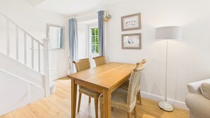 A dining area with a wooden table and wicker chairs, a floor lamp, and framed pictures on the wall. - Host & Stay | Dove Cottage (Warkworth)