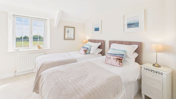 A bedroom with two beds, a window with a view, a bedside table with a lamp, and framed pictures on the wall. - Host & Stay | Dove Cottage (Warkworth)