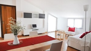 Uma sala de estar moderna com área de jantar, um sofá branco, um tapete vermelho e uma TV em um suporte.