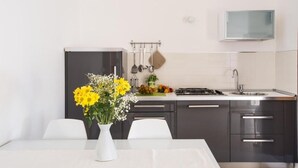 Uma cozinha moderna com mesa de jantar, cadeiras brancas, um vaso de flores e uma TV instalada acima da pia.