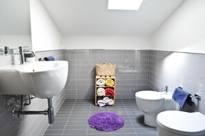 Un baño con dos lavamanos, un bidé y una alfombra morada en el suelo.