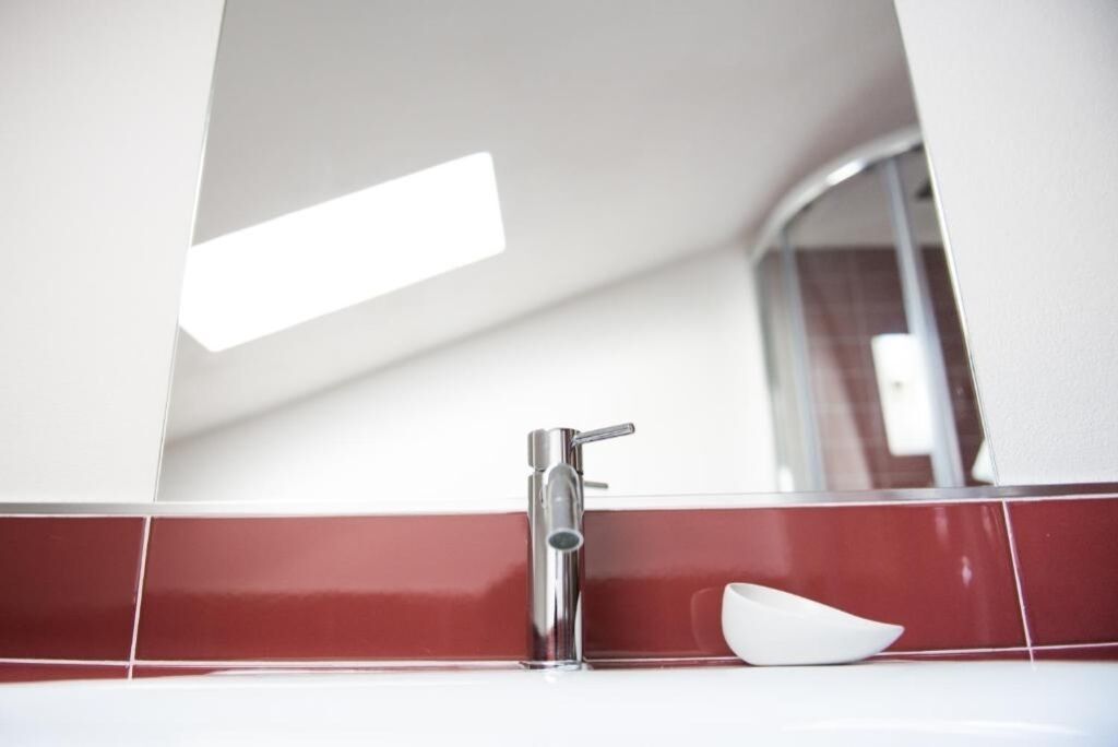 Un baño con un grifo moderno, un lavamanos blanco y un salpicadero de azulejos rojos.
