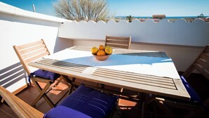 Um terraço com mesa de madeira, cadeiras e uma tigela de frutas.
