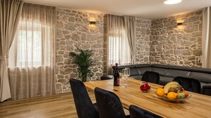 A dining area with a stone wall, wooden table, black leather seating, and a fruit bowl. - Villa Mila - Makarska by Villas Guide (Zmijavci)