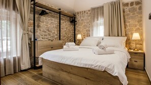 A bedroom with a stone wall, wooden bed frame, white bedding, and two bedside lamps. - Villa Mila - Makarska by Villas Guide (Zmijavci)