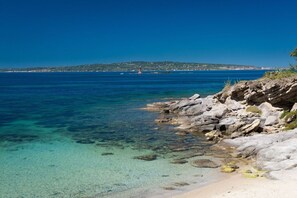 A coastal scene with clear waters, rocky shoreline, and a distant island with buildings.