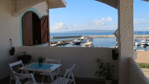 A balcony with a view of a marina, white chairs, a small table, and potted plants.