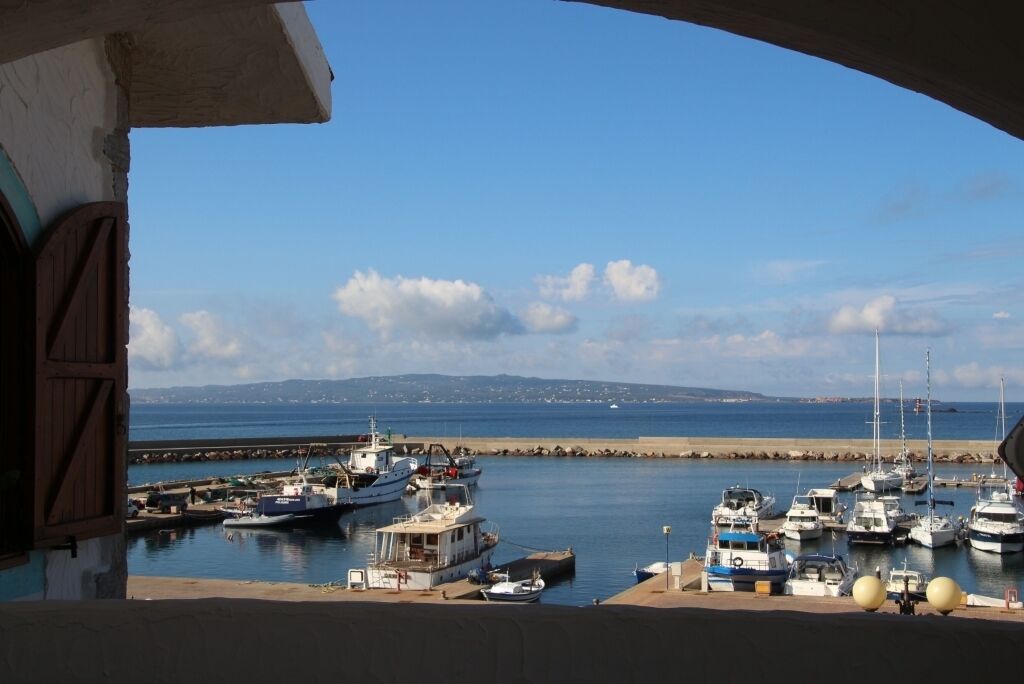 Marina com barcos atracados, céu claro e paisagem distante da costa.