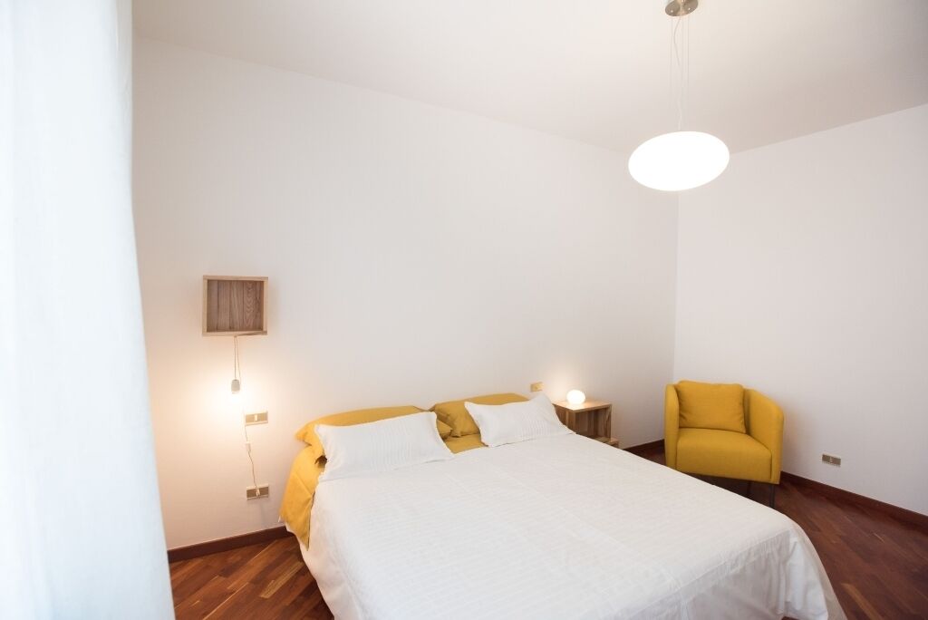 A bedroom with a bed, a nightstand, a lamp, and a chair.