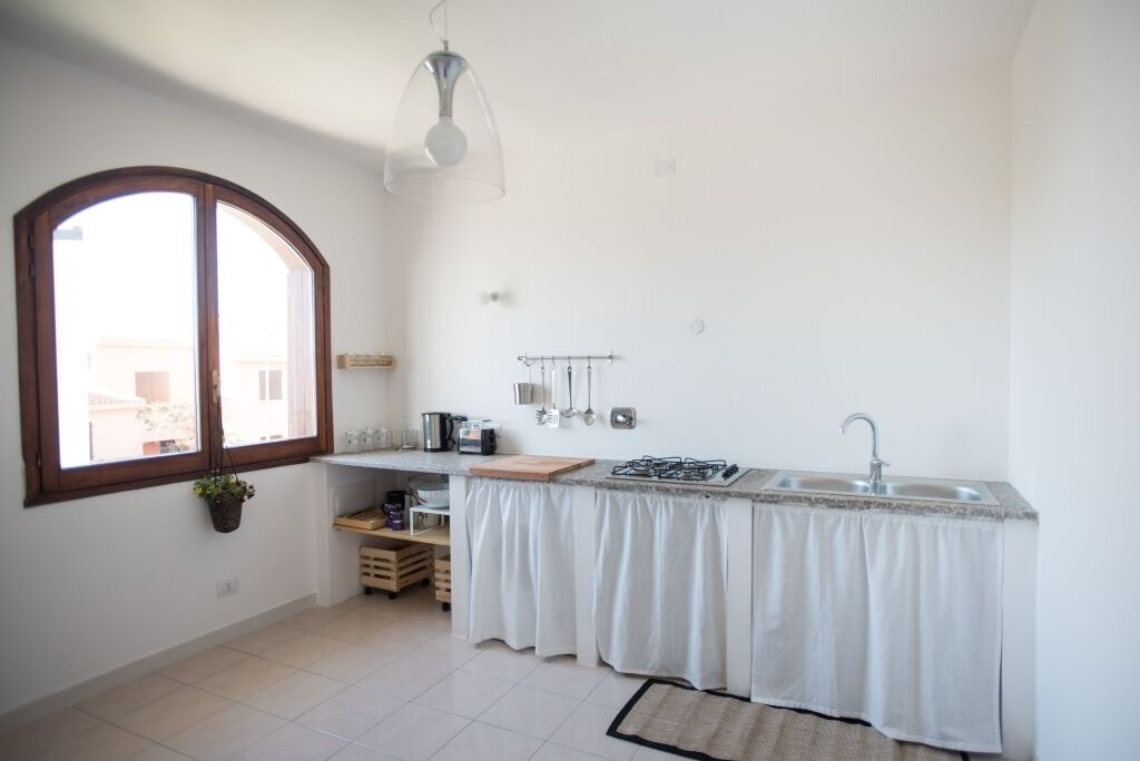 Une petite cuisine lumineuse, dotée d’une fenêtre, d’un luminaire suspendu et d’un plan de travail avec un évier.