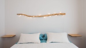 A bed with white and blue bedding, two white pillows, and a wooden headboard with string lights.