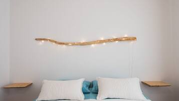 Cama com roupa de cama branca e azul, duas almofadas brancas e cabeceira de madeira com luzes de cordão.