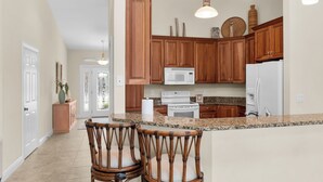 A kitchen with wooden cabinets, a white refrigerator, a microwave, and a stove. There are two wicker chairs at the island. - Waterfront 3 Bed Playground in Paradise Awaits (Marco Island)